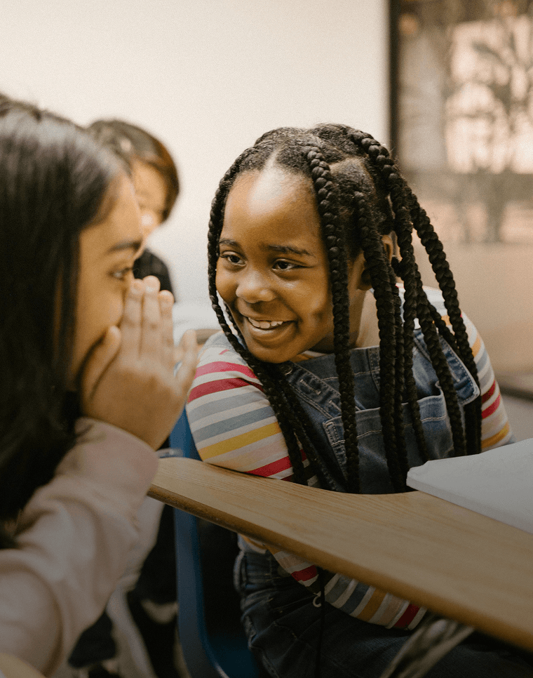 Los estudiantes sonrientes susurran entre ellos mientras aprenden un nuevo idioma en la escuela.